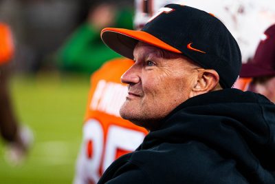 A man wearing a Virginia Tech hat stands on the sidelines during a football game