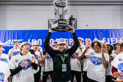 A person wearing a hat hoists a trophy